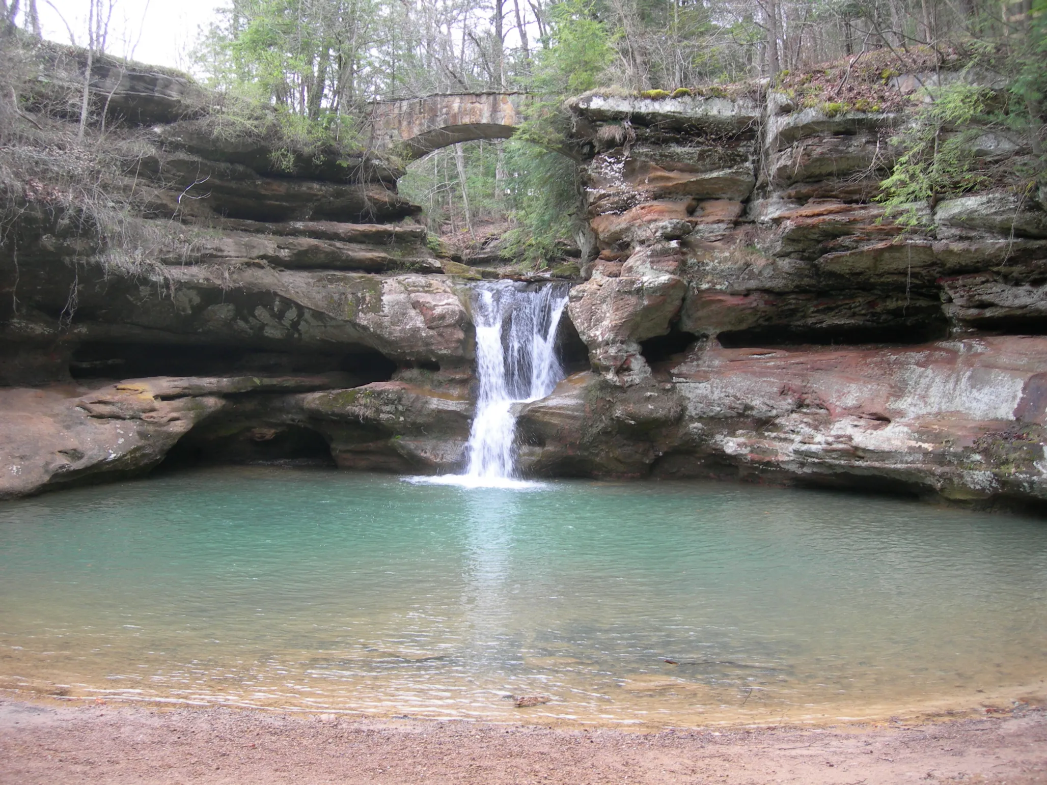 Small waterfall down a short rocky cliff into a green-blue lake at North Country National Scenic Trail