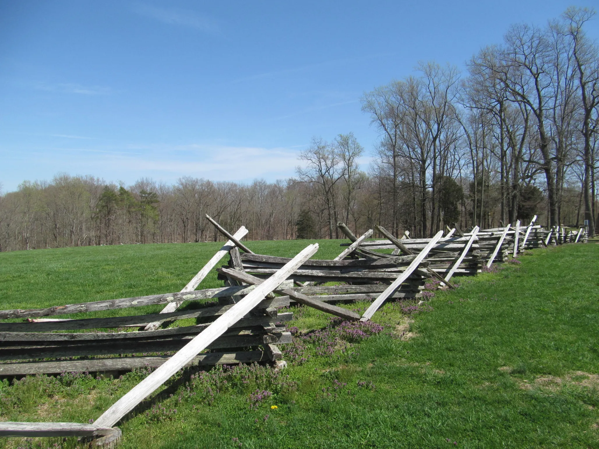 A wooden fence zig-zags across a green field. In the distance