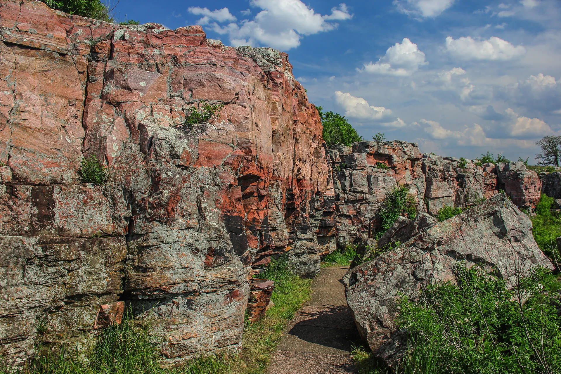 a red rock wall with white fluffy clouds in a blue sky