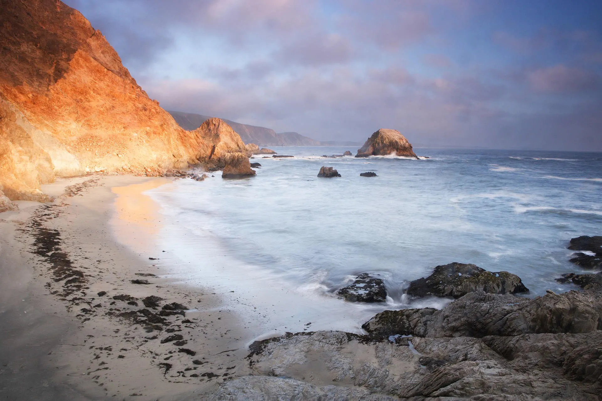 sun shines on rugged beach where ocean meets mountainside