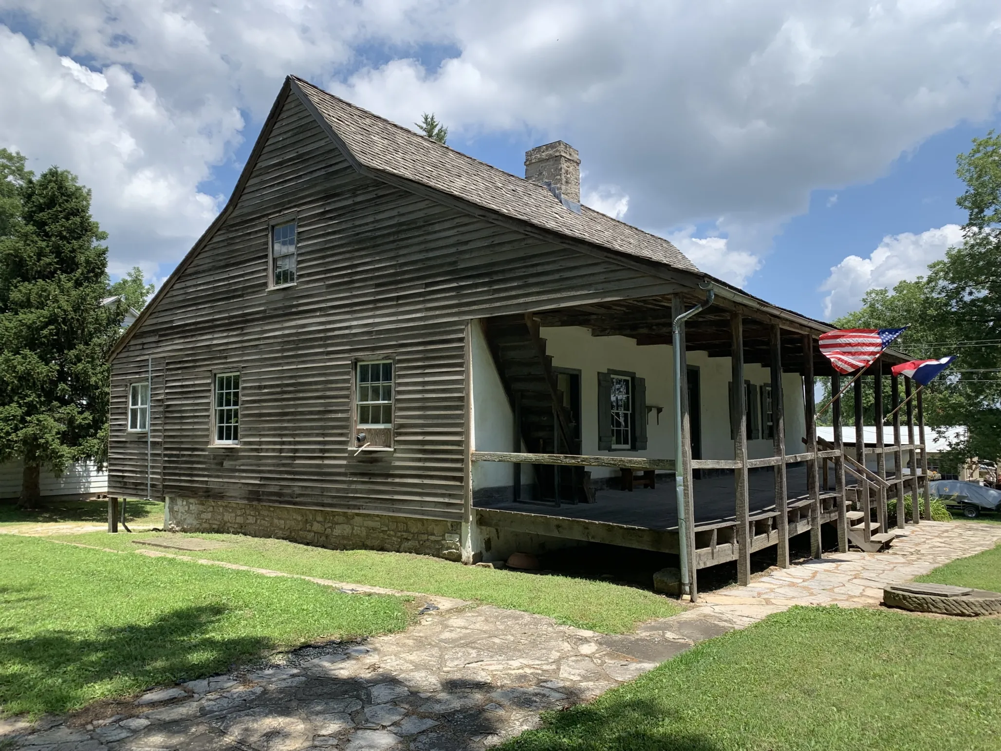 Wood frame house with triangular roof and U.S. and French flags flying in front