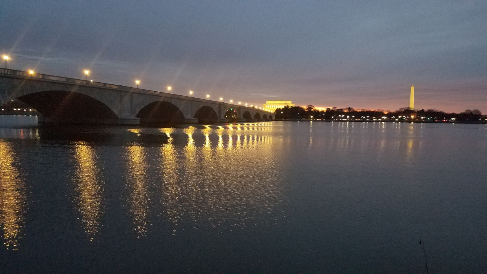 Arlington Memorial Bridge dim light with lights reflecting off of water and memorials in the distance