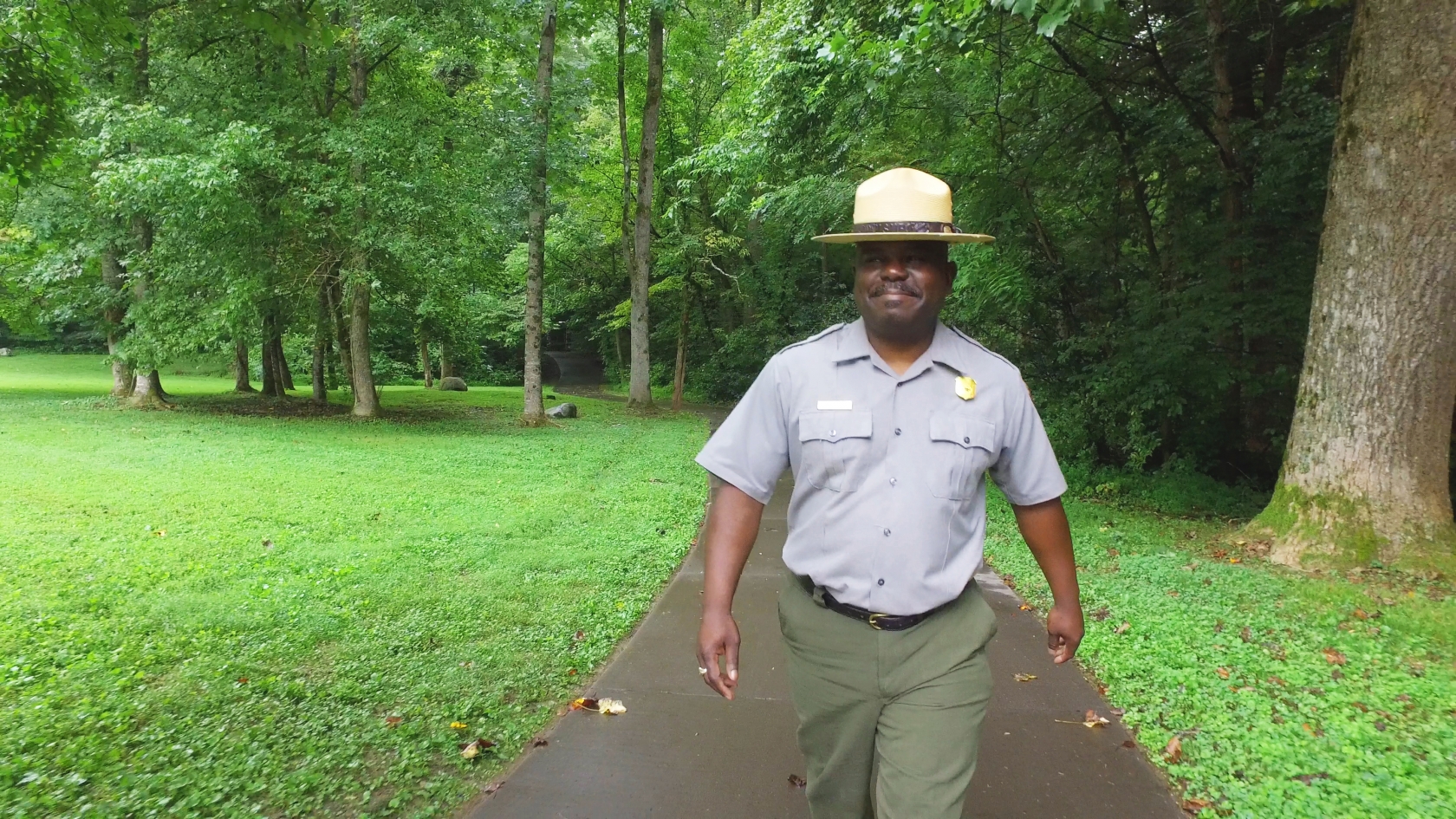 El superintendente Cassius Cash viste un uniforme de guardaparques y camina por un sendero boscoso