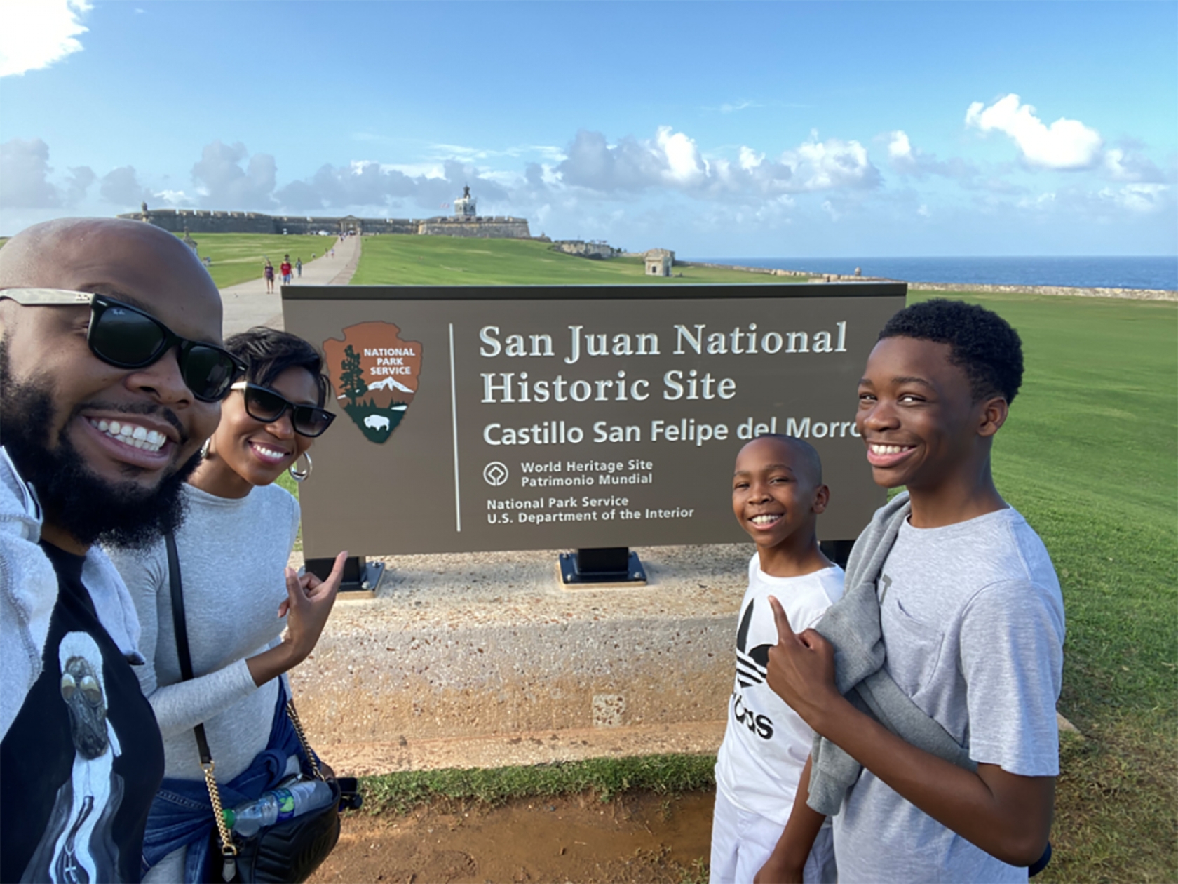 Kev on Stage y su familia posan frente al cartel del parque en el Sitio Histórico Nacional de San Juan