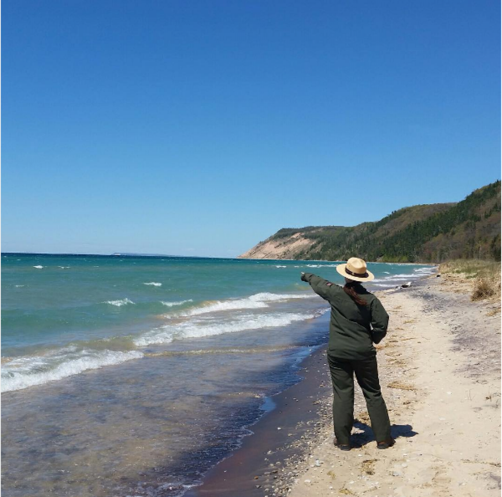 Park Ranger pointing at the shores of Lake Michigan and dunes at Sleeping Bear National Park 