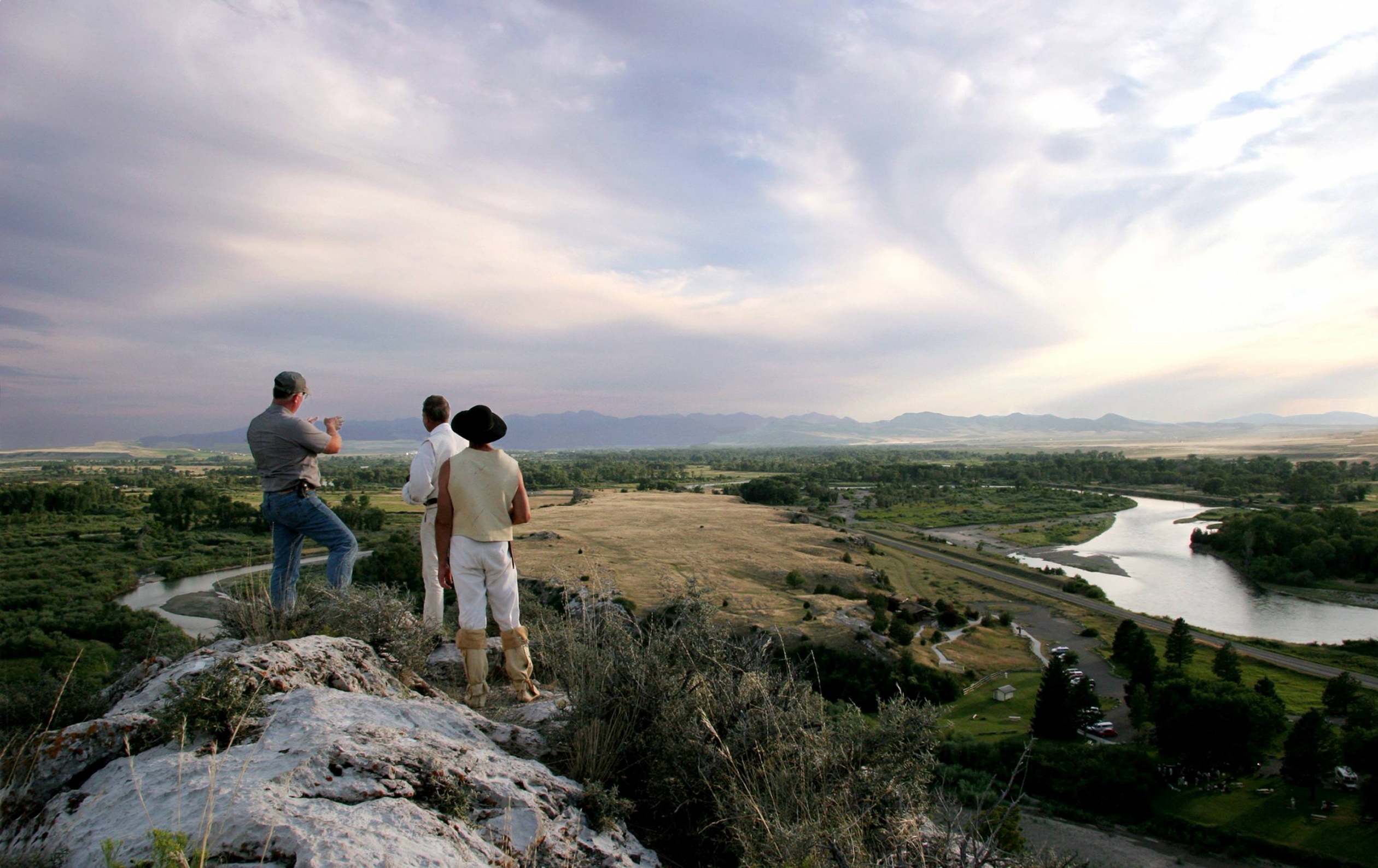 Three men looking out across a green valley with a river running through it from a rock outcrop along the Lewis & Clark National Historic Trail