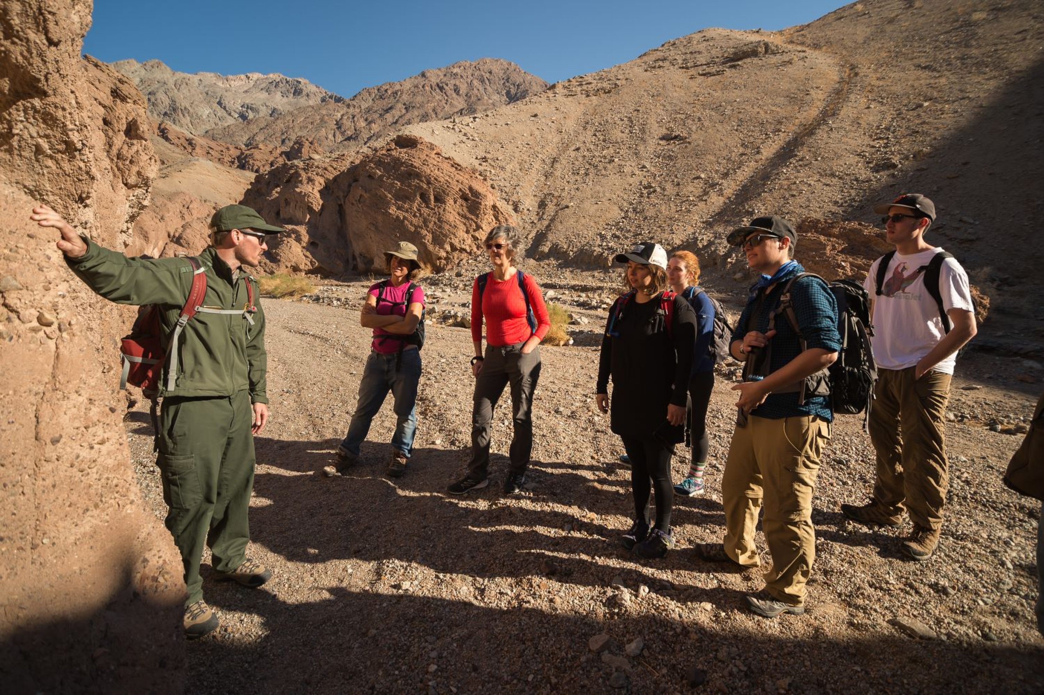 A group of visitors watching as a park ranger points to something in the rocks on the paleontology tour at Death Valley National Park