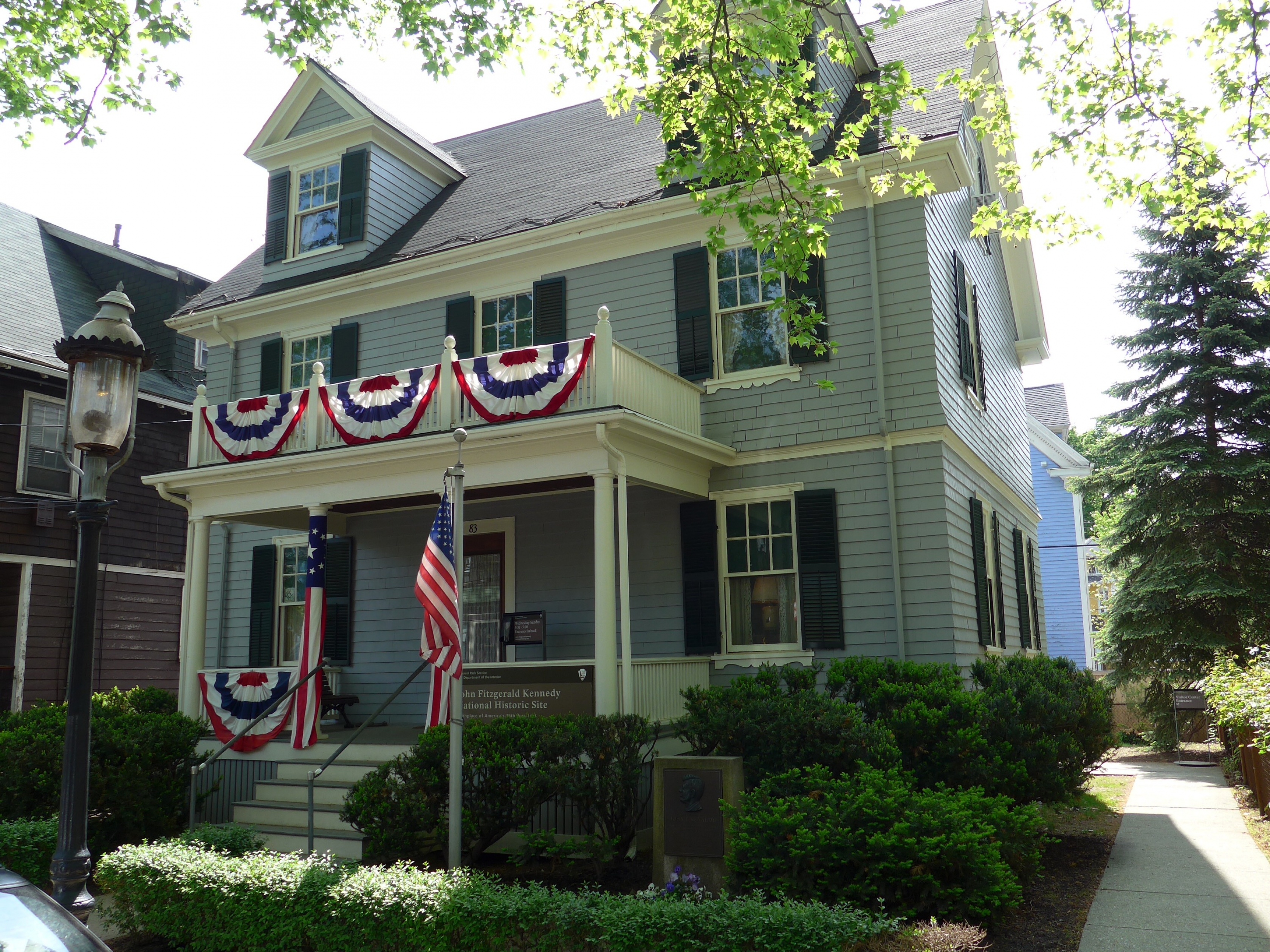 The front of the two-story house with red, white, and blue half-circle flags adorning the banisters at John F. Kennedy National Historic Site