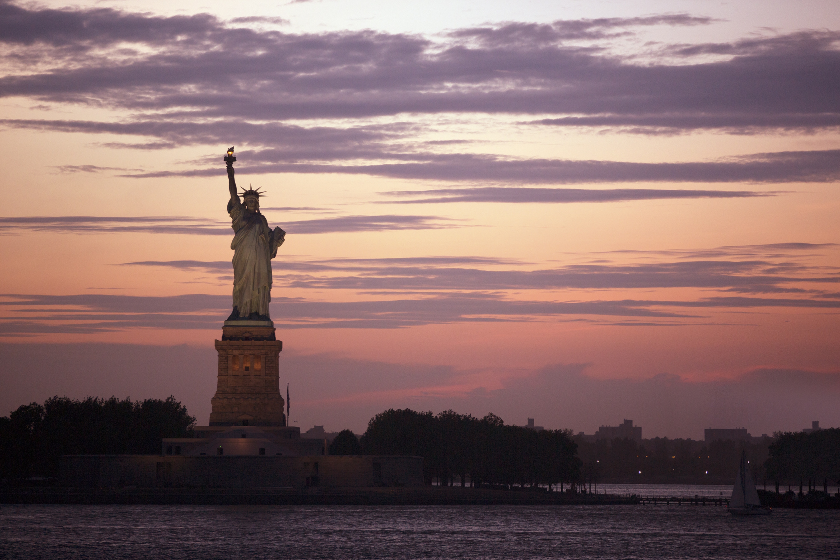 colorful red and orange sunset with purple clouds behind a dimly lit Statue of Liberty