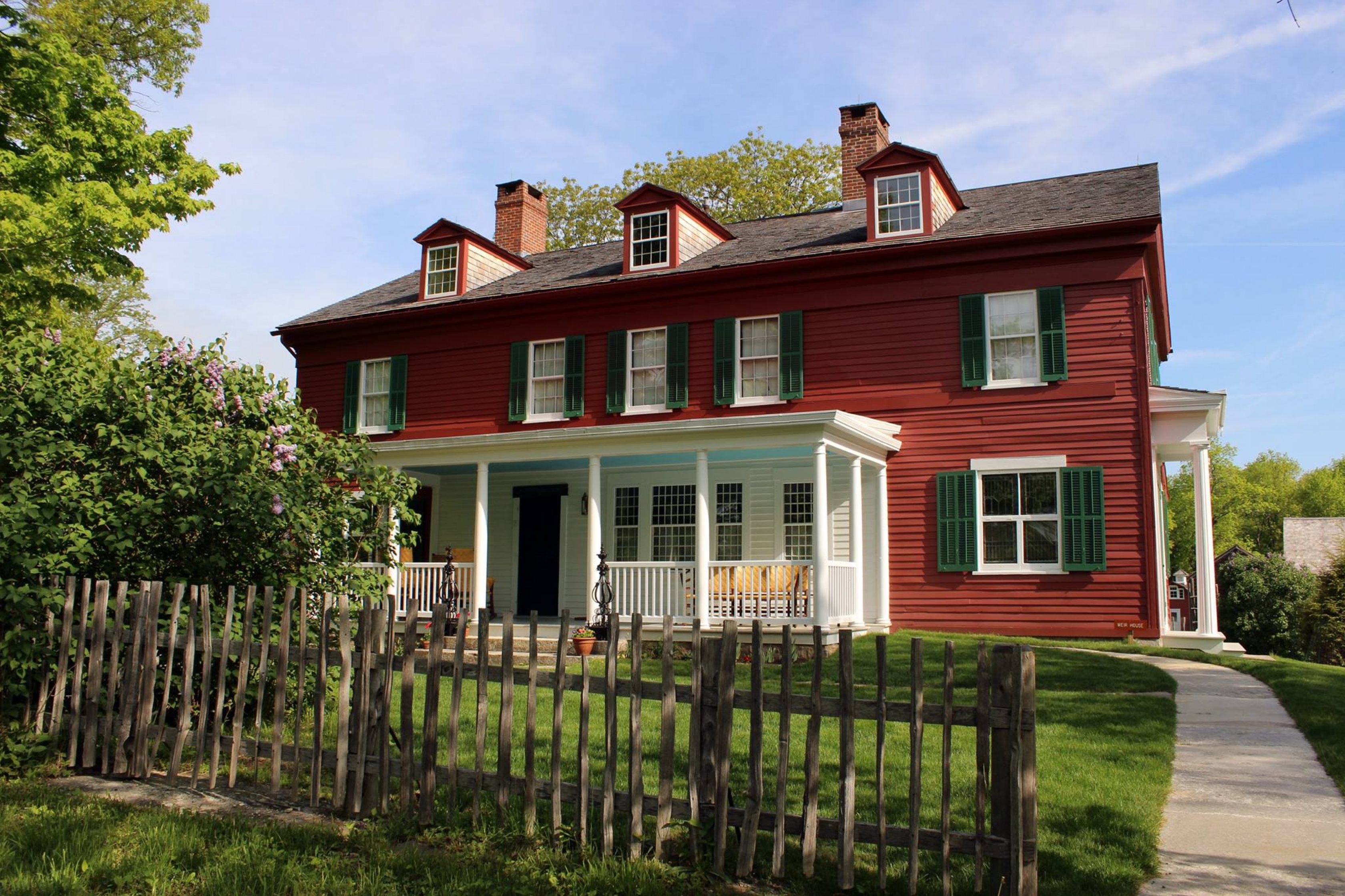 casa roja con un persianas verdes ventanas blancas detrás de una valla de madera y césped verde en la granja del vertedero Sitio Histórico Nacional