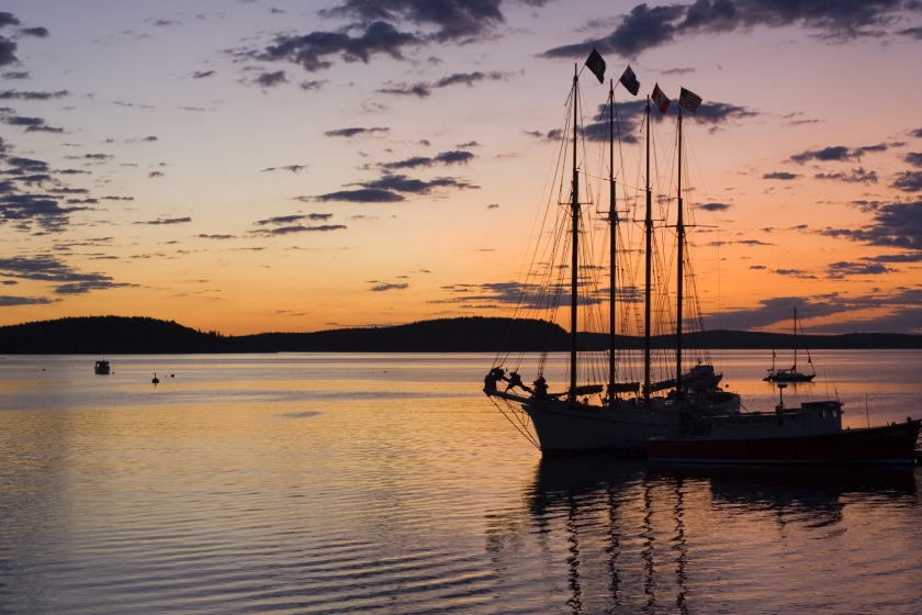 Colorful sunset with the silhouette of a 3-masted sailboat docked at Acadia National Park