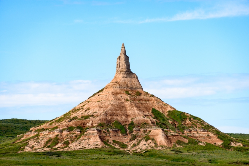 A large, orangey brown rock formation, shaped like a funnel or "chimney" reaches into the sky