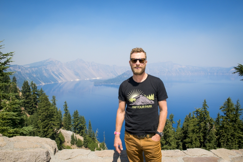 Dierks Bentley wearing a black Find Your Park shirt standing in front of Crater Lake National Park