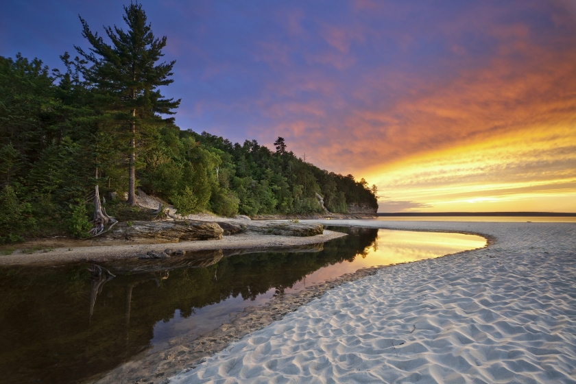 Rugged forest coastline of Pictured Rocks National Park with offset sandbar and sunset reflecting on lake