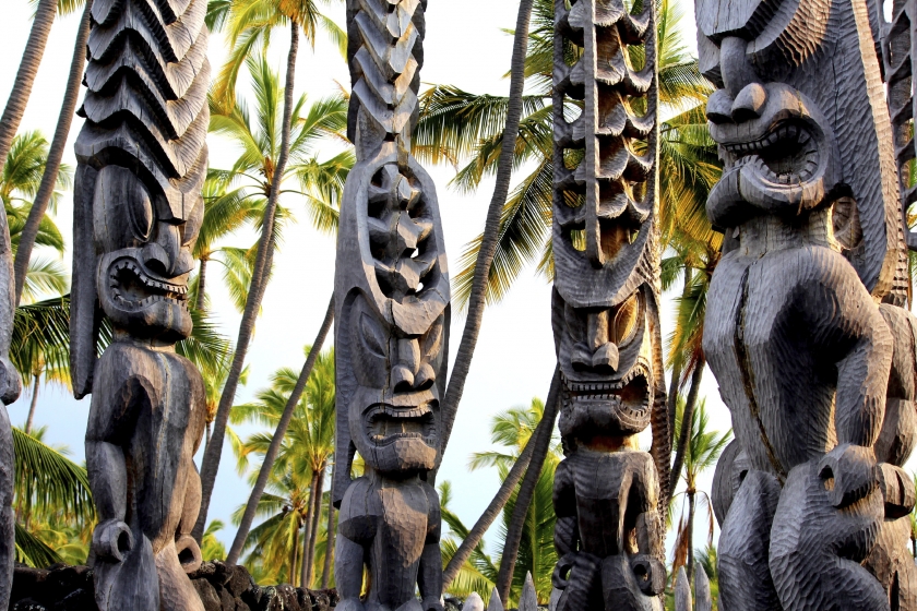 Four sun-lit wooden totems with carved faces at Pu'uhonua National Park