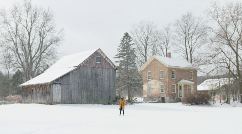 A visitor walks in the snow between a barn and two story brick building